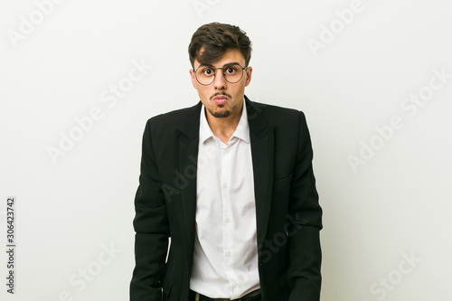 Young business hispanic man shrugs shoulders and open eyes confused.