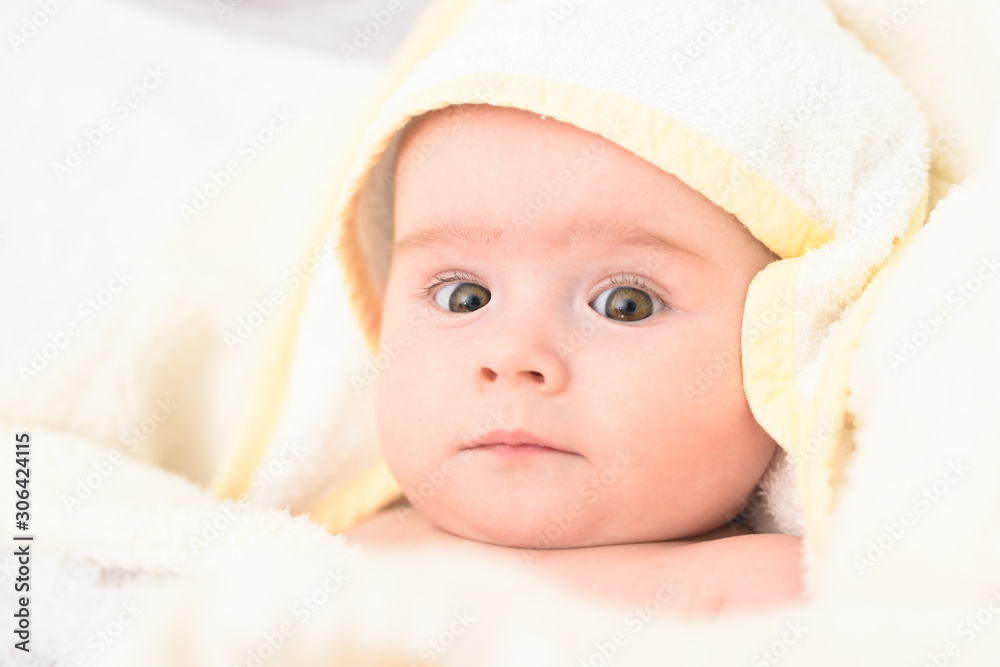 Adorable 6 months old Baby girl infant on a bed on her belly with head up looking into camera with her big eyes. Natural light. Adorable 6 months old Baby girl infant on a bed on her belly with head up looking into camera with her big eyes. Natural light.