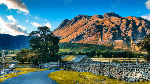 Picturesque stone cottage house next to a river with Great Langdale mountains and valley in the background at sunset time in the Lake District National Park in North West England, UK.