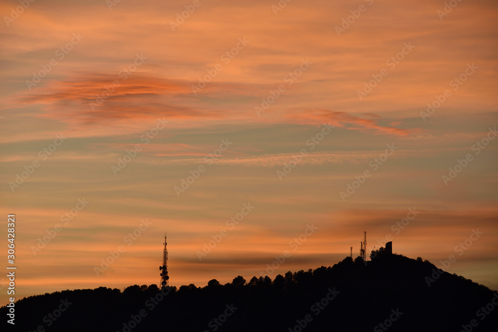 Silhouette of a telecommunications tower and another historic stone on a hill at sunset