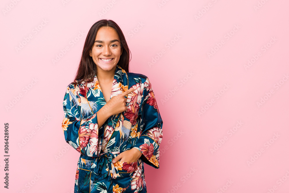 Young indian woman wearing a kimono pajama smiling and pointing aside, showing something at blank space. Young indian woman wearing a kimono pajama smiling and pointing aside, showing something at blank space.