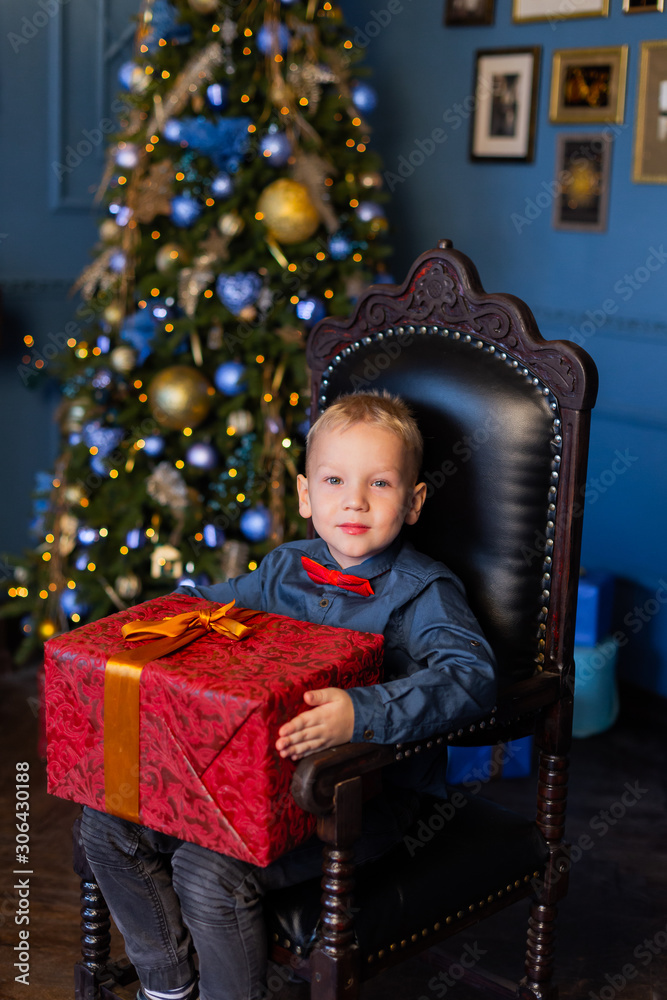 Beautiful boy sits on a chair in New Year's decor with a gift in his hands.