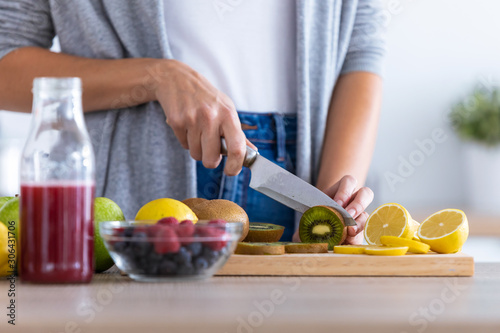 Woman s hands while she cutting kiwi over wooden table in the kitchen.