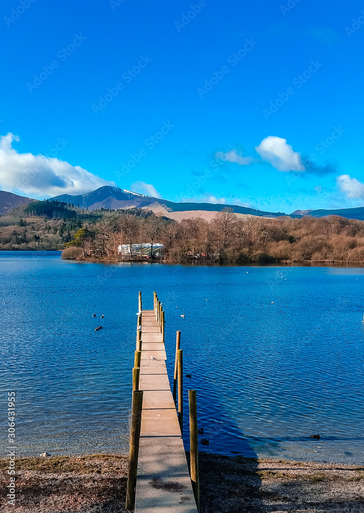 Wooden pier in Keswick town in the Lake District surrounded by mountains like Skiddaw and Derwentwater lake on a peaceful sunny day. 