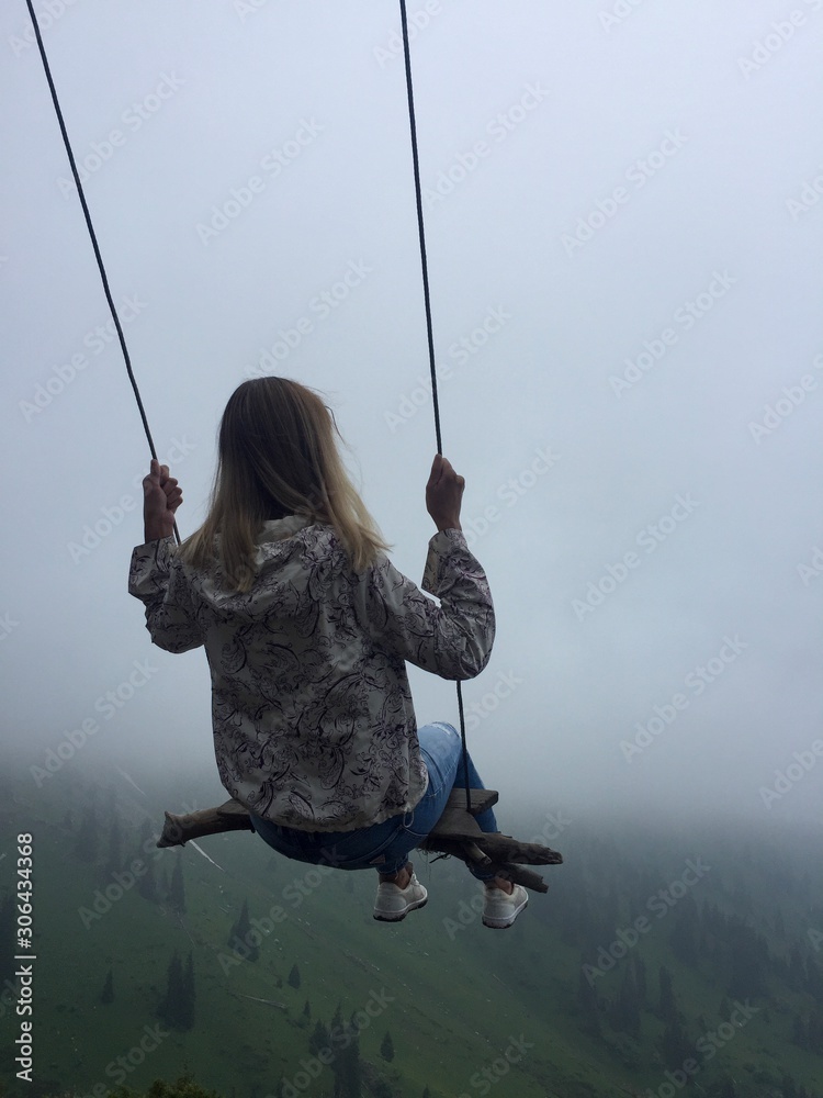 girl with blond hair sitting on a swing in the fog over the precipice, challenge. Kazakhstan, Alma-ATA. Welcome to Kazakhstan!sport lifestyle