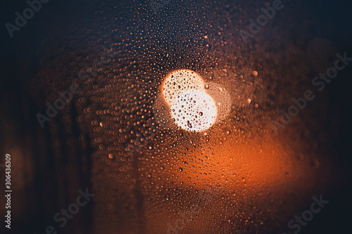 Wet window with raindrops over city glowing lights at background. Autumn season. Rainy weather.
