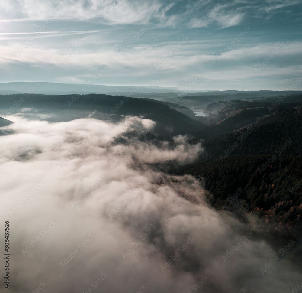 Fog and clouds in the valley of a mountain lake. Flying over a mountain nature landscape with view from above. Harz Mountains