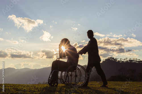 Sad pensioner sitting in wheelchair with his wife at sunset.