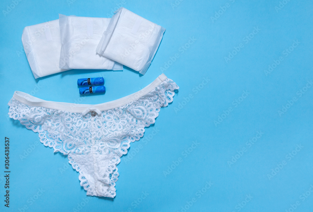 Obraz premium 1 women's white lace panties, sanitary swabs, pads on blue background