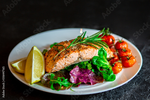 Salmon steak with lettuce, cherry tomatoes and lemon slices. Gala dinner. Food for lunch. Grilled red fish. Baked salmon in the oven