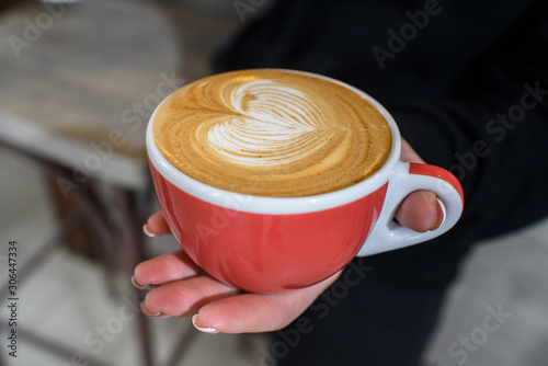 Delicious and fragrant cappuccino in the hand of a barista girl in a cozy coffee shop