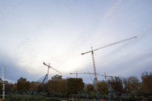 Group of cranes on a construction site in the city center of Vienna, Austria, in front of a building being assembled taken from afar during a cloudy evening, under a grey sky