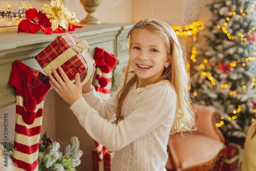 Cute teen girl with present near Christmas tree smiiling photo