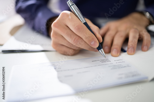 Close Up Of Businessman Filling Blank Cheque At Desk