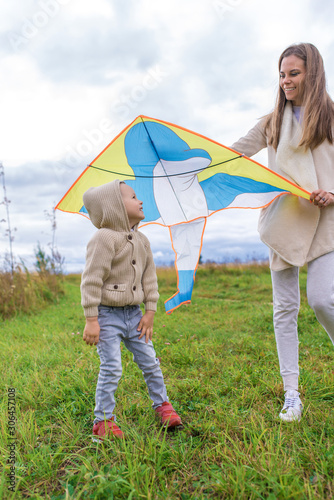 Happy family, young mother woman, little boy son 3-6 years old, emotions delight joy positive. Beige casual wear. They launch kite, laugh relax weekend. Warm casual wear, beige sweater with hood.