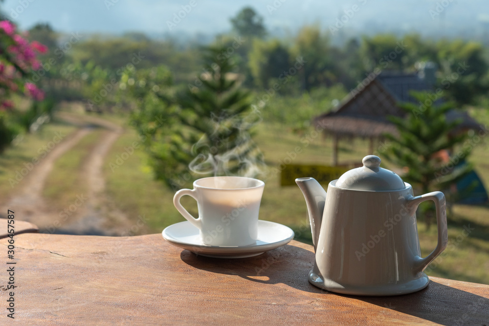 cup of coffee with white coffee mug on wooden table with scenery of mountain and field of plants in background