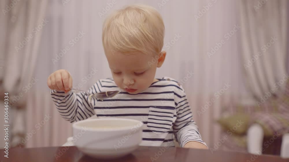 Baby eating. Cheerful baby child eats food itself with spoon. Portrait of beautiful child having breakfast at home. Cute child eating breakfast at home. Baby eating. Cheerful baby child eats food itself with spoon. Portrait of beautiful child having breakfast at home. Cute child eating breakfast at home.