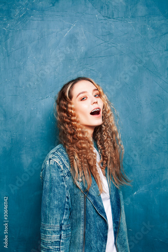young pretty hipster girl with curly hair posing emotonal on blue wall background, lifestyle people concept