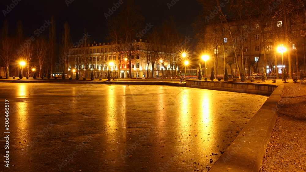 Smolensk, Russia, autumn evening in Park Lopatin Garden, beautiful ice Pond and quay with glowing street lights on house background