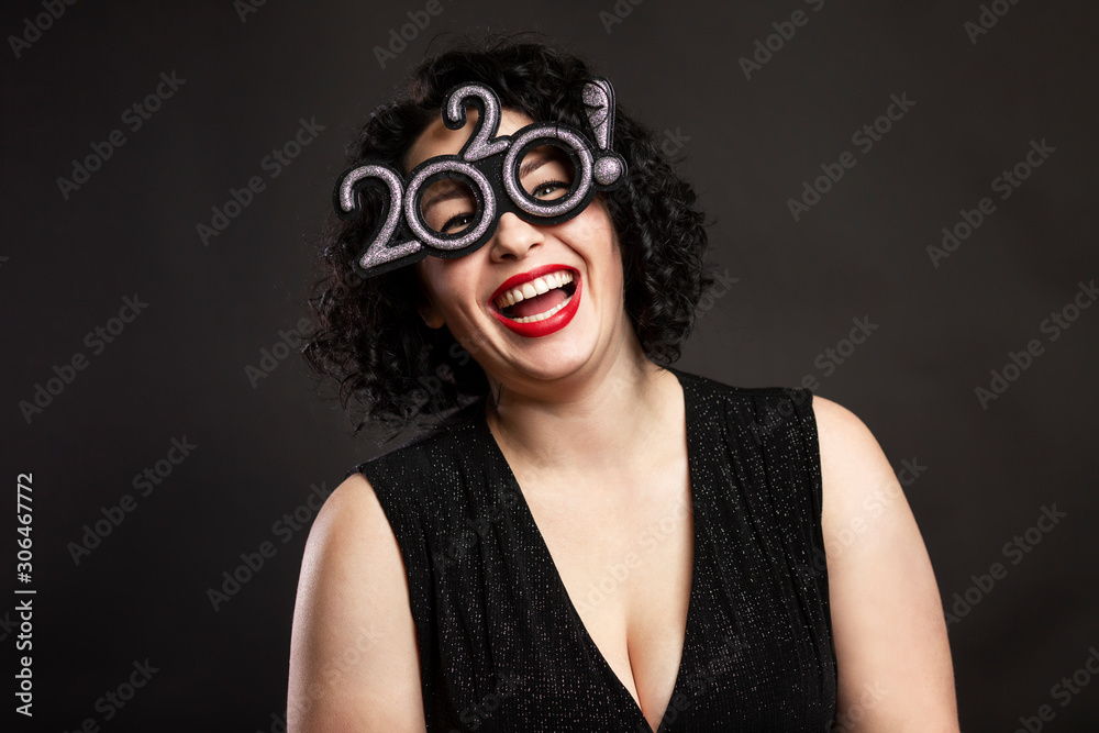 Young beautiful woman is laughing. Brunette with curly hair and red lips. Festive New Year mood. Black background. Close-up.