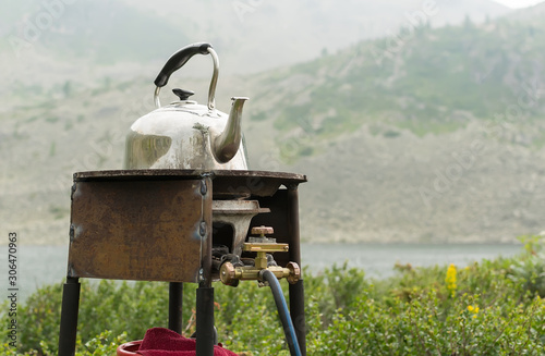 tourism, household classic old teapot stands and basks on a homemade rusty metal gas burner on the background of a large mountain with a large slope and a lake photo