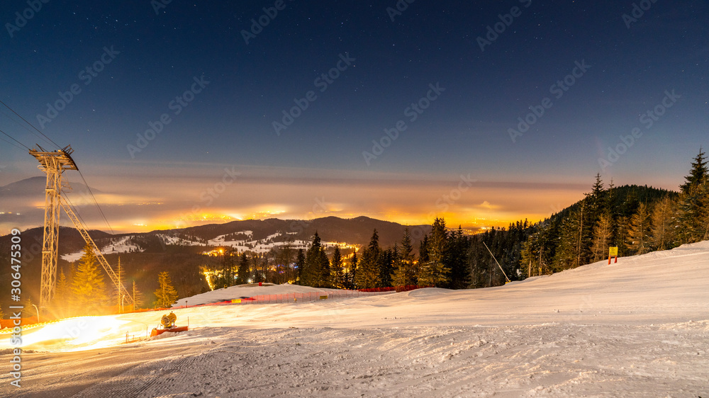 Poiana Brasov, Romania. Postavarul Peak. Panorama of a groomed snow and forest ski in winter resort. Dark scenery at night long exposure.