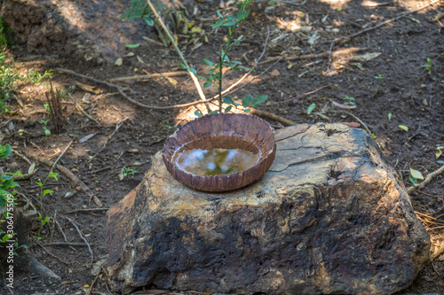Water in a small handmade clay bowl isolated on top of a large rock image in horizontal format with copy space