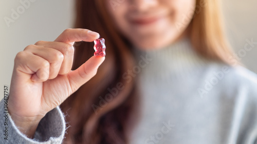 Closeup image of a beautiful woman holding and looking at a red jelly gummy bear photo
