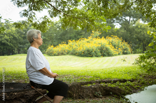 Asian senior woman very calm in green nature at park,meditation can have a role in treating anxiety, depression and pain,female elderly sit upright with right hand on left her,meditation,healthy life 