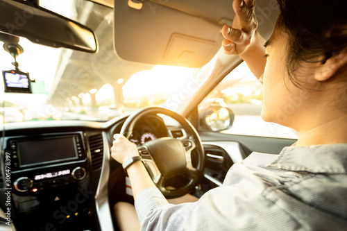 Asian female driver covering face by hand of bright sun,disturbed dazzled by sun light,difficulty in driving,young woman driving car feeling hot uncomfortable,risk of eye damage from ultraviole,UV ray