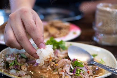 Close up fingers hand eating sticky rice Spicy minced pork salad in white dish, dipping sauce mix pork herb spicy thai style traditional Isan (Northeastern Thailand)
