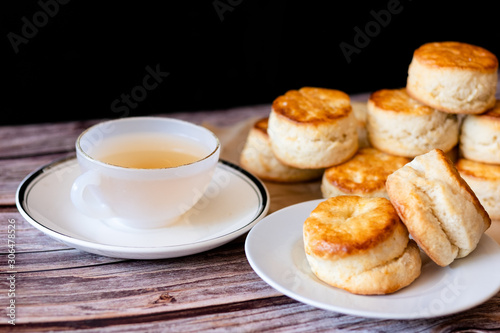 White cup of hot tea and Fresh Homemade delicious butter scones on wooden table with black background. Traditional British Scones perfect combination for tea time.