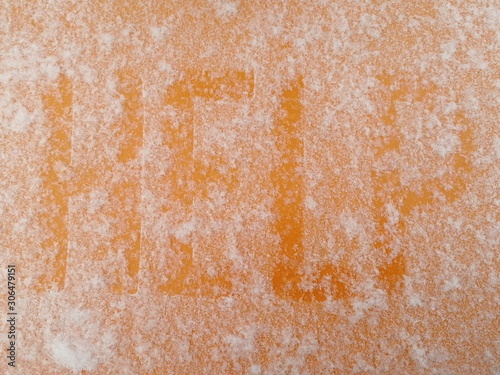 Word snow covered HELP written by hand on an orange metal surface covered with hoarfrost. View from above.