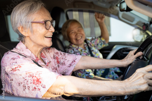 Happy asian senior female driver in her car,enjoy traveling during retirement age with her friend,healthy old people having fun,laughing together,elderly woman driving car,road trip,travel concept