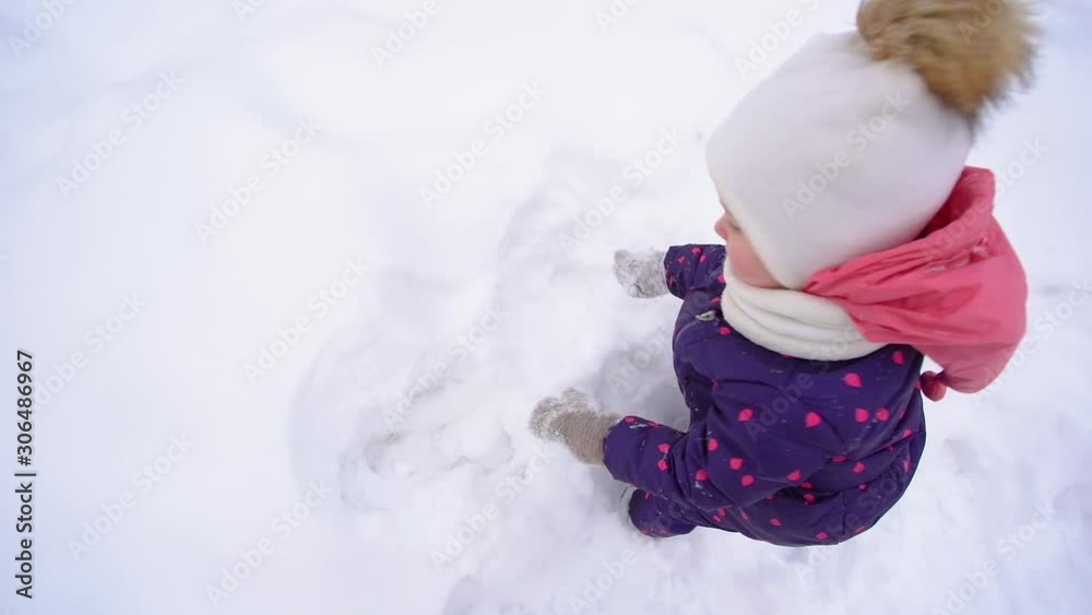 Closeup top view of cute little baby girl playing happily in white fluffy fresh snow outdoor in winter. Slow motion full hd video footage.