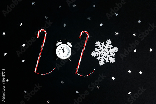 2020 made from candy canes, alarm clock and snowflake on black background.