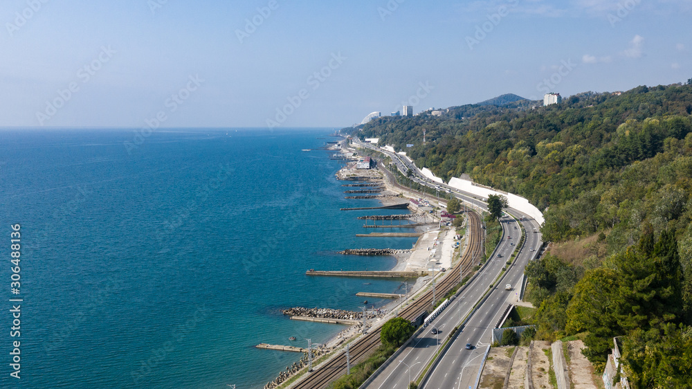 Aerial photography photo. The road along the seashore. Russian resort city of Sochi. Green trees. Blue sea. Beach strip. Railway along the seashore. Bird's eye view