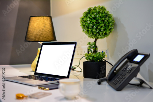 Office desk with blank screen laptop and phone