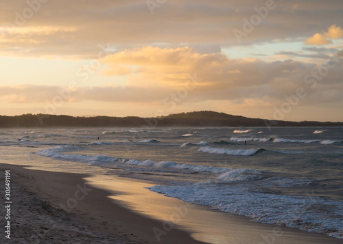 River mouth feeding into the ocean at dusk with surfers catching the last few waves of the day