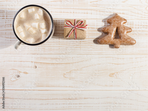 Hot Christmas drink with marshmallows in an iron mug and gingerbread cookies, on a white table. New Year, holiday background, copy space.