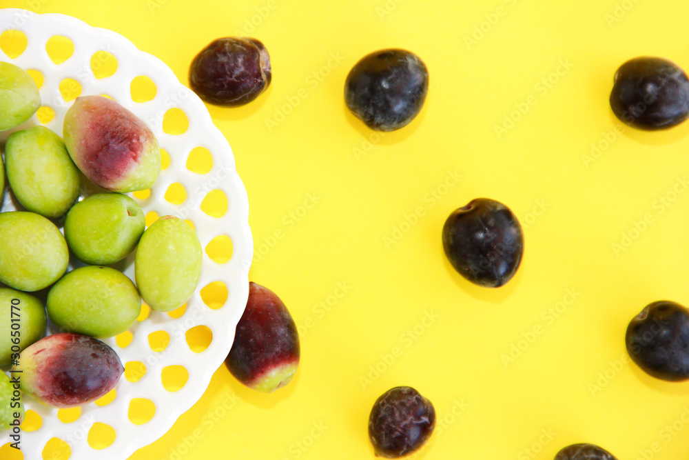 natural round green and brown olives in a decorative plate on a yellow background