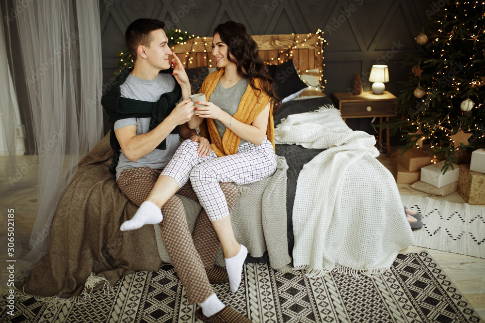 happy couple in love in the morning on the bed near the Christmas tree, hug, Christmas morning. home clothes and sweaters. comfort and warmth of hearts