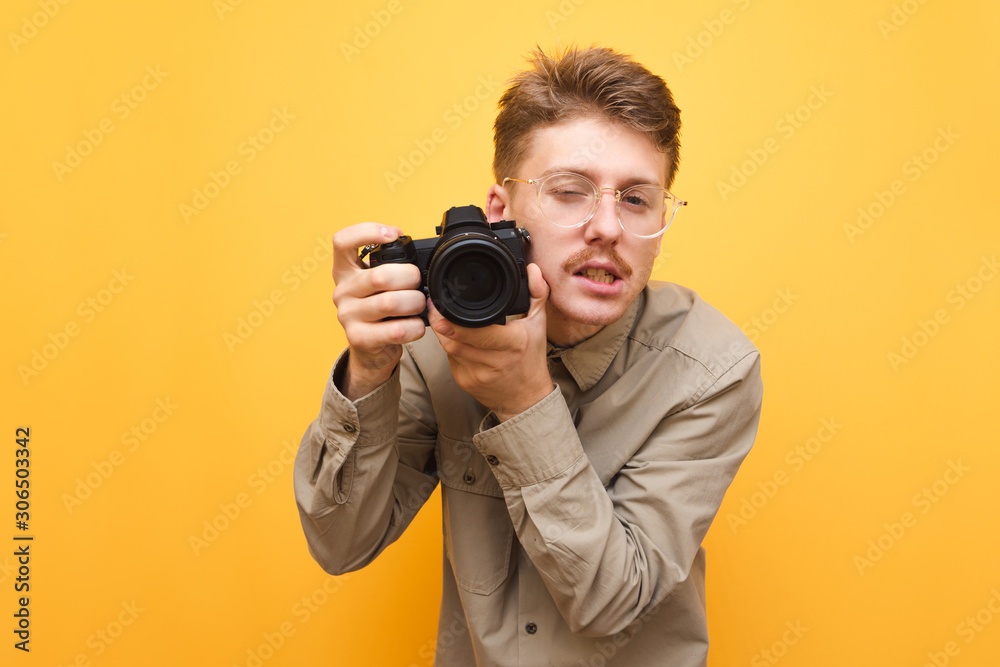 Funny young photographer with mustache and glasses isolated with camera in  hand on yellow background, looking into camera with sexy face and taking  photo. Portrait of a cheerful stock photographer Stock Photo |