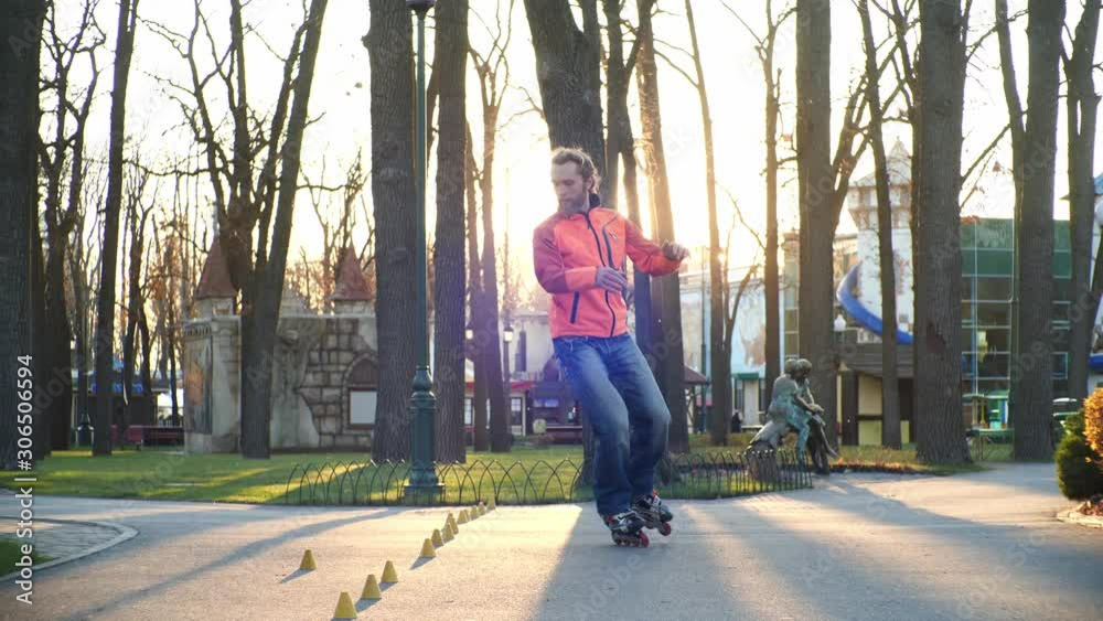 Training of a professional roller who skillfully skates in the central park of the city and performs complex turns between training cones. Active and healthy lifestyle. Side view in slow motion. Training of a professional roller who skillfully skates in the central park of the city and performs complex turns between training cones. Active and healthy lifestyle. Side view in slow motion.