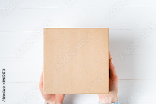 Square cardboard box in female hands. Top view, white background © somemeans