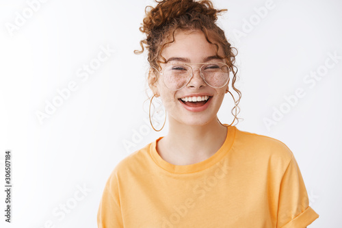 Charismatic carefree young 20s redhead girl wearing glasses smiling laughing out loud hear funny joke talking chatting friends students lunch break campus, standing white background orange t-shirt