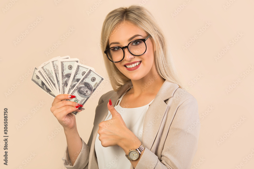 Fototapeta premium beautiful young woman in a suit on a beige background with dollars in hand