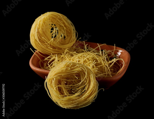 Dry, raw egg pasta noodles and clay pot isolated on black background photo