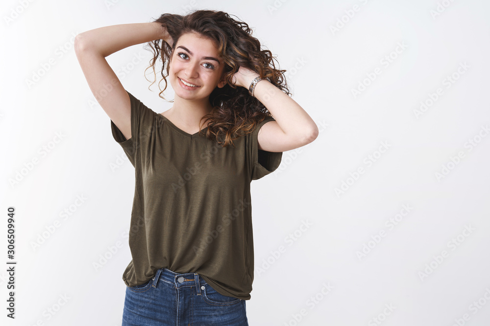 Joyful young carefree armenian girl playing curly hair comb, hold hands behind smiling joyfully making hairstyle near mirror, standing casually white background wearing olive t-shirt jeans