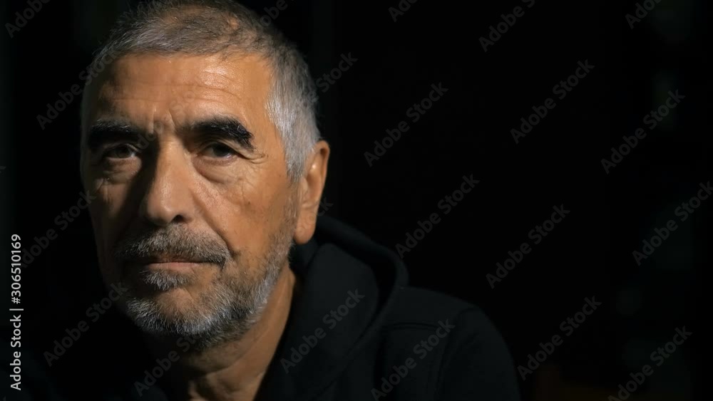 Serious confident mature man in the dark,opening his closed eyes,looking camera 